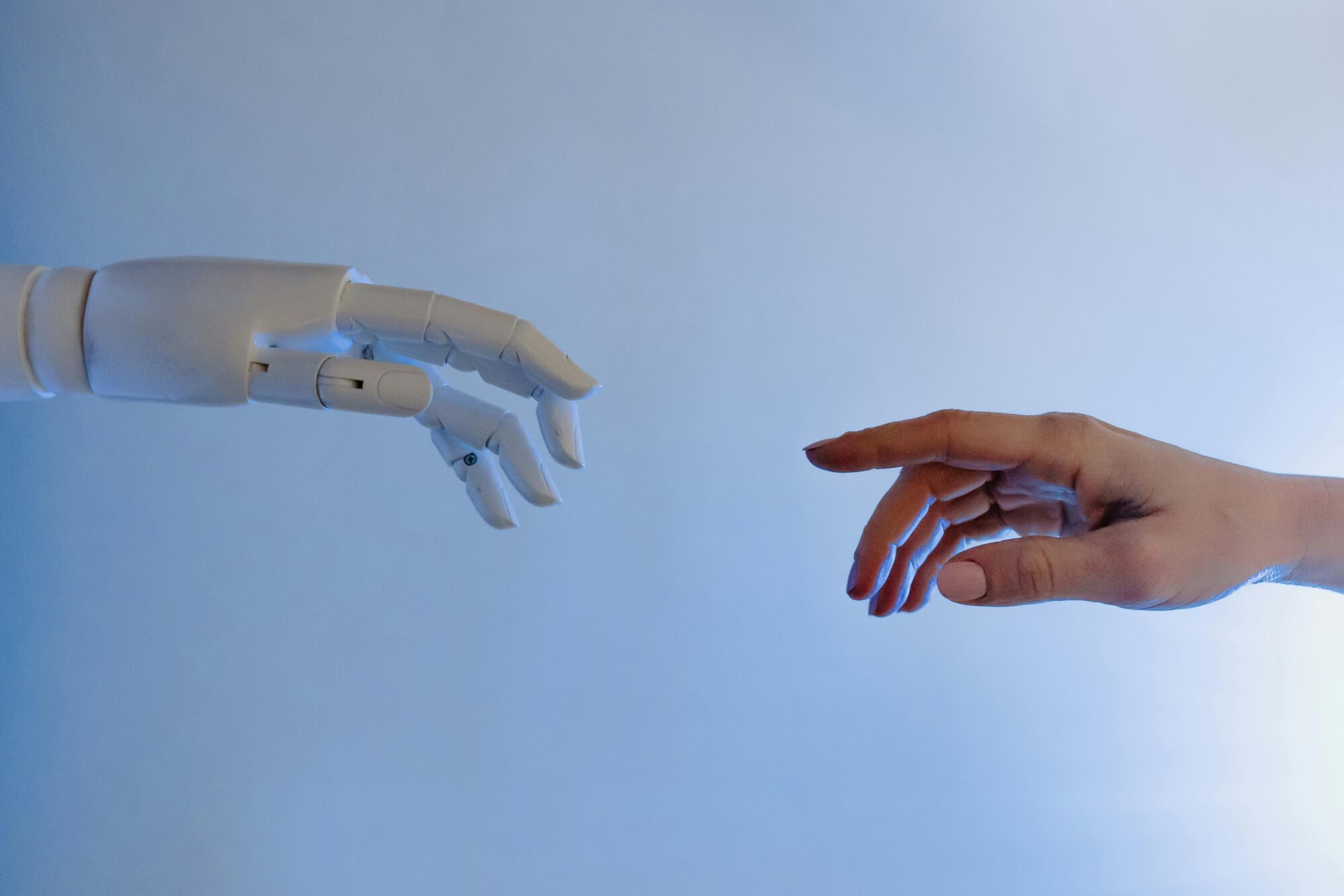 Human hand and robot hand reaching toward each other against a blue sky, symbolising the relationship between people and AI technology