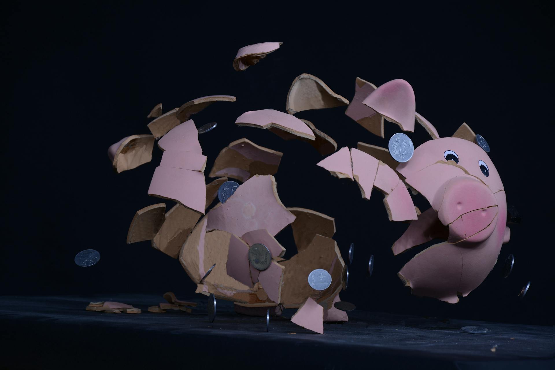 Shattered pink piggy bank with coins scattering - you cannot save yourself rich