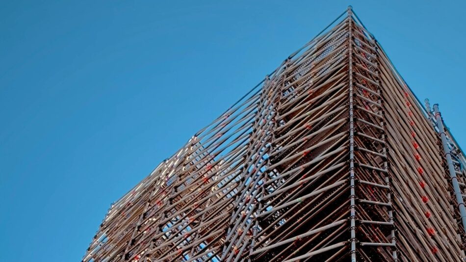 Tall scaffolding against a clear blue sky — the structural support that lets a building stand.