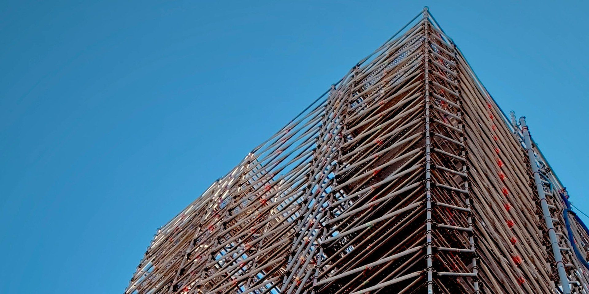 Tall scaffolding against a clear blue sky — the structural support that lets a building stand.